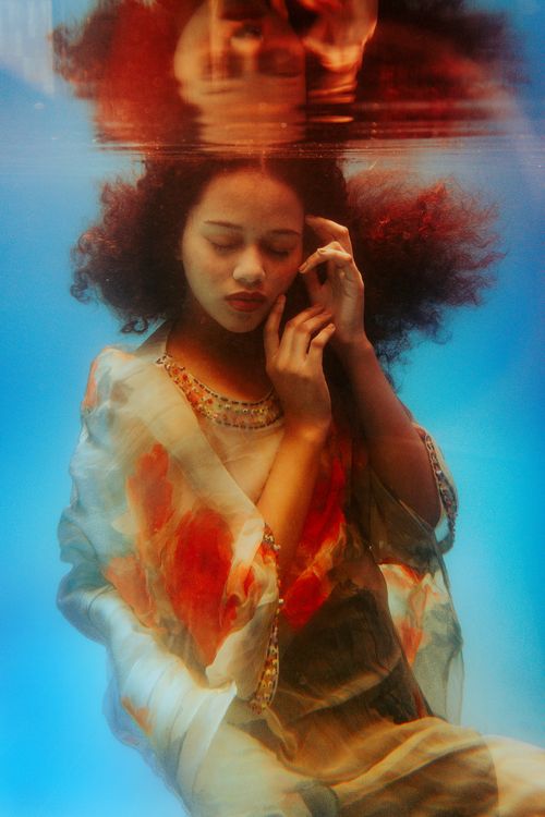 Free Underwater of calm red hair female with eyes closed wearing loose dress while touching face gently in blue seawater Stock Photo