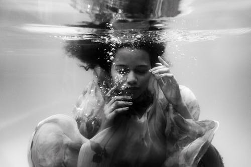 Free Black and white unemotional young female in loose dress diving with eyes closed into seawater Stock Photo