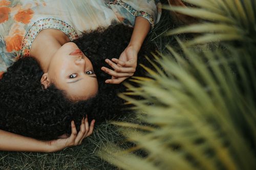 Free From above pretty ethnic female in stylish dress lying gracefully on grassy meadow in exotic garden and looking at camera calmly Stock Photo