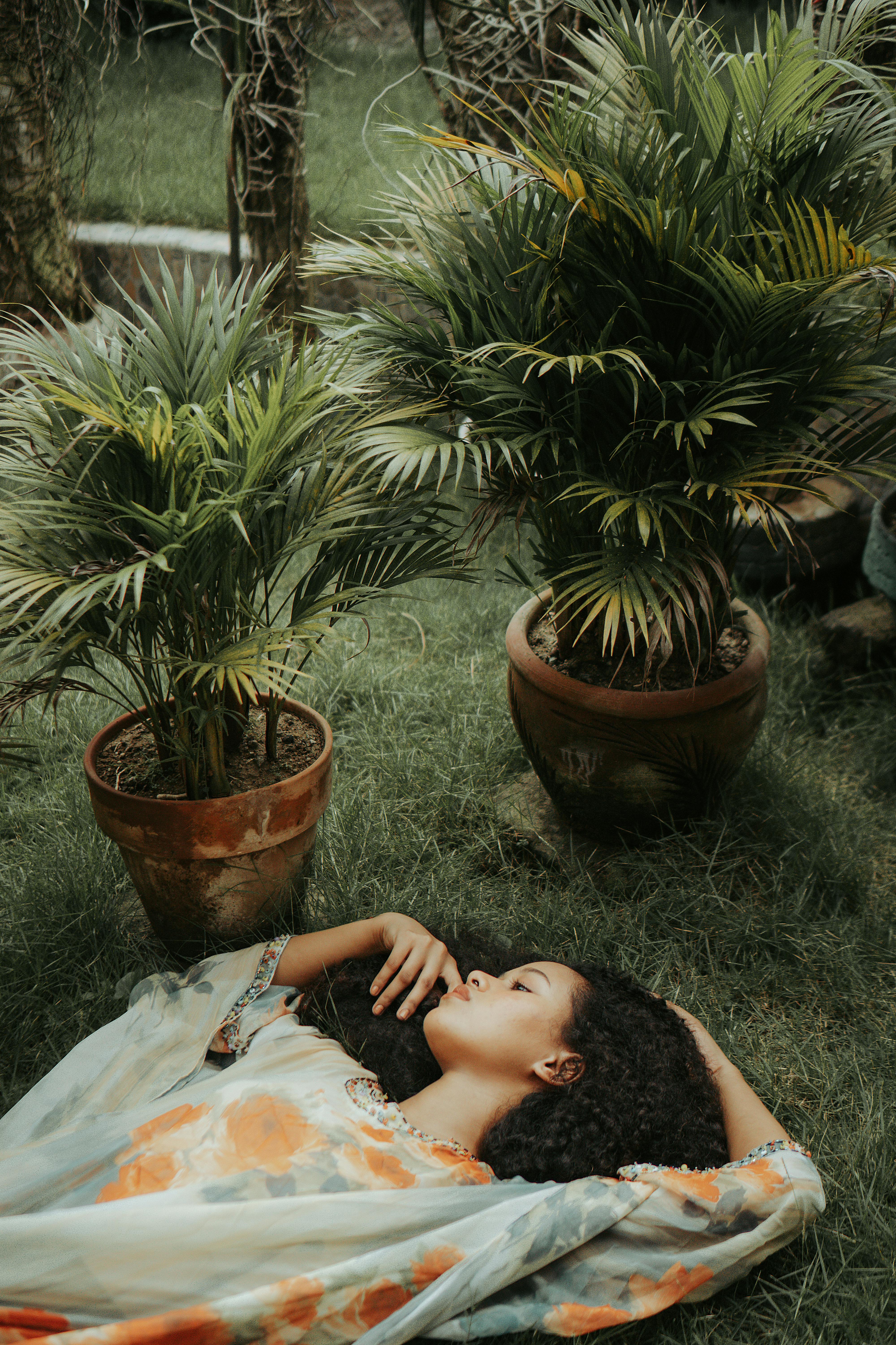 From above elegant charming ethnic female with black curly hair lying gracefully on green garden meadow and touching lips gently
