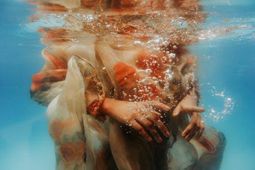 Underwater shot of crop unrecognizable female wearing summer dress diving into clean seawater