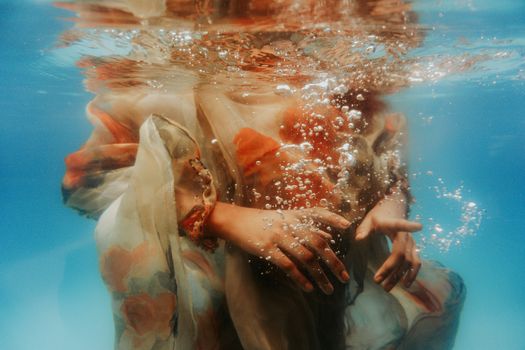 Underwater shot of crop unrecognizable female wearing summer dress diving into clean seawater