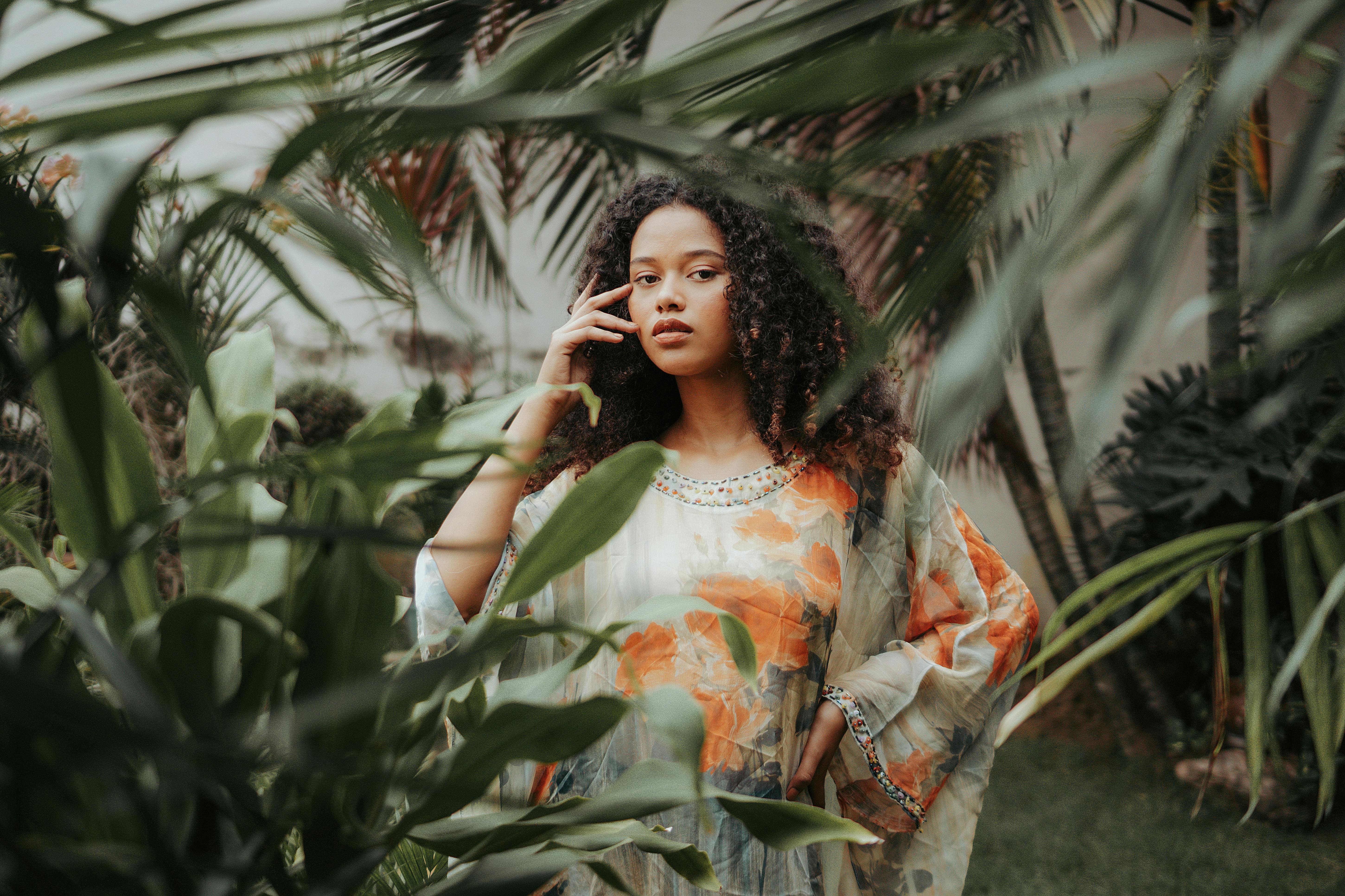 A serene portrait of a stylish woman amidst tropical plants, exuding beauty.