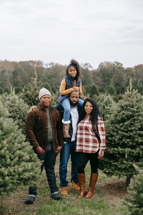 Smiling black family standing close among fir trees