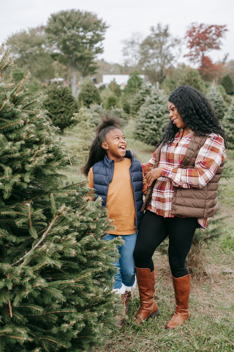 Happy Black Mother And Daughter Standing Near Fir Tree