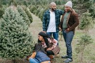 Positive African American dad standing with teen son while females sawing spruce for family Christmas celebration