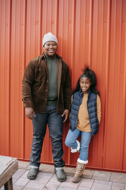 Smiling black siblings near metal fence in daylight