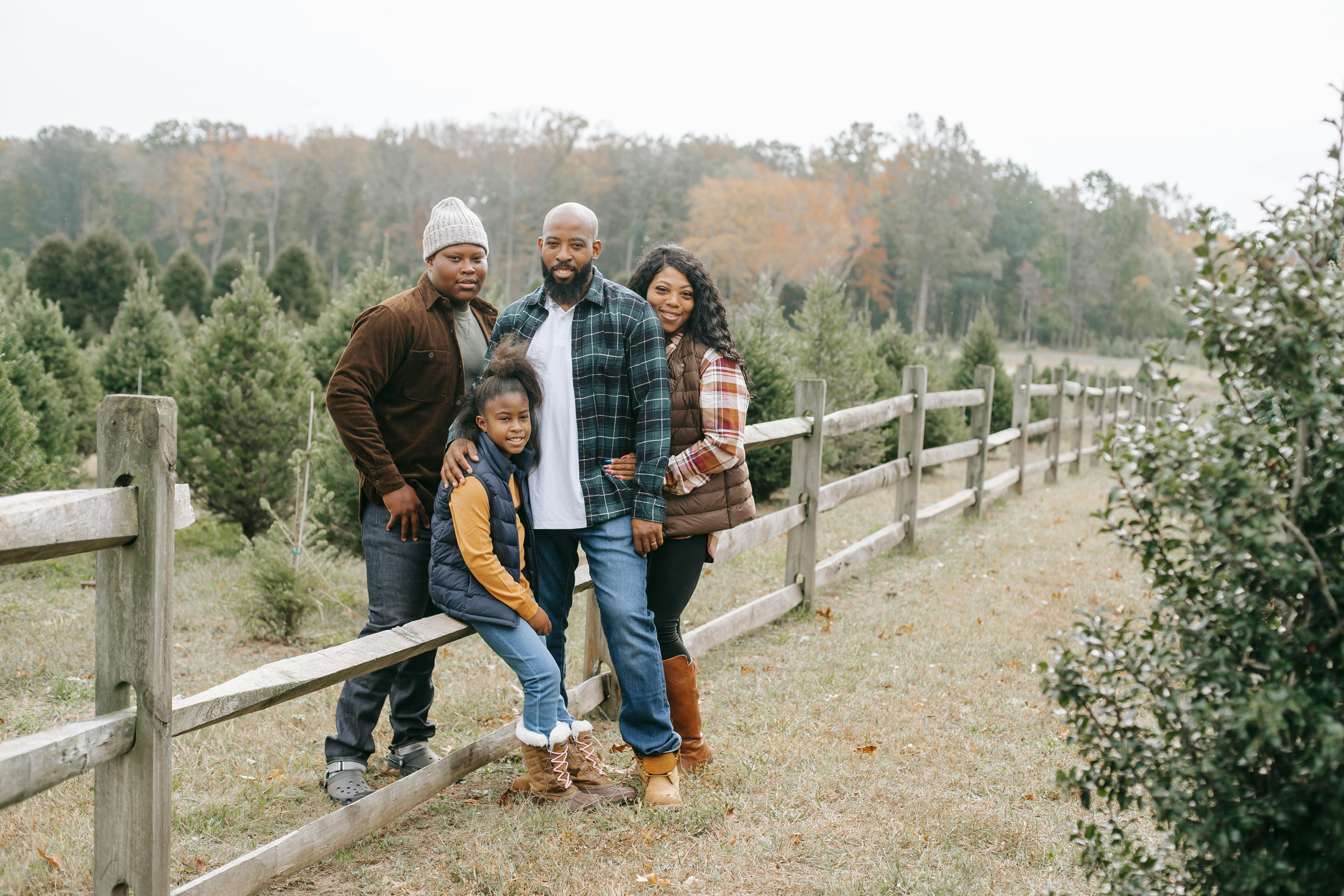 smiling black family embracing near fence in countryside