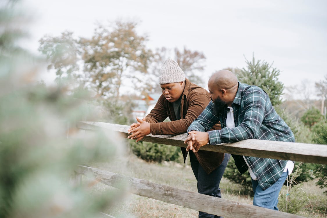 Free Black father conversing with teenager near fence on farmland Stock Photo