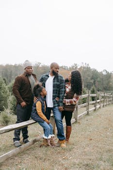 Young African American parents with teenager and girl speaking near fence on farm under white sky