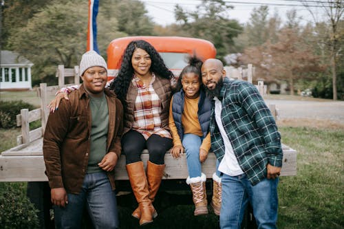 Cheerful African American family embracing near vehicle on farm