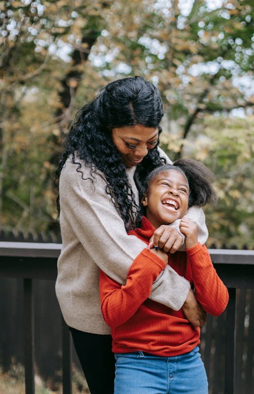 Free African American woman embracing gently cheerful girl in casual wear in countryside in daytime Stock Photo