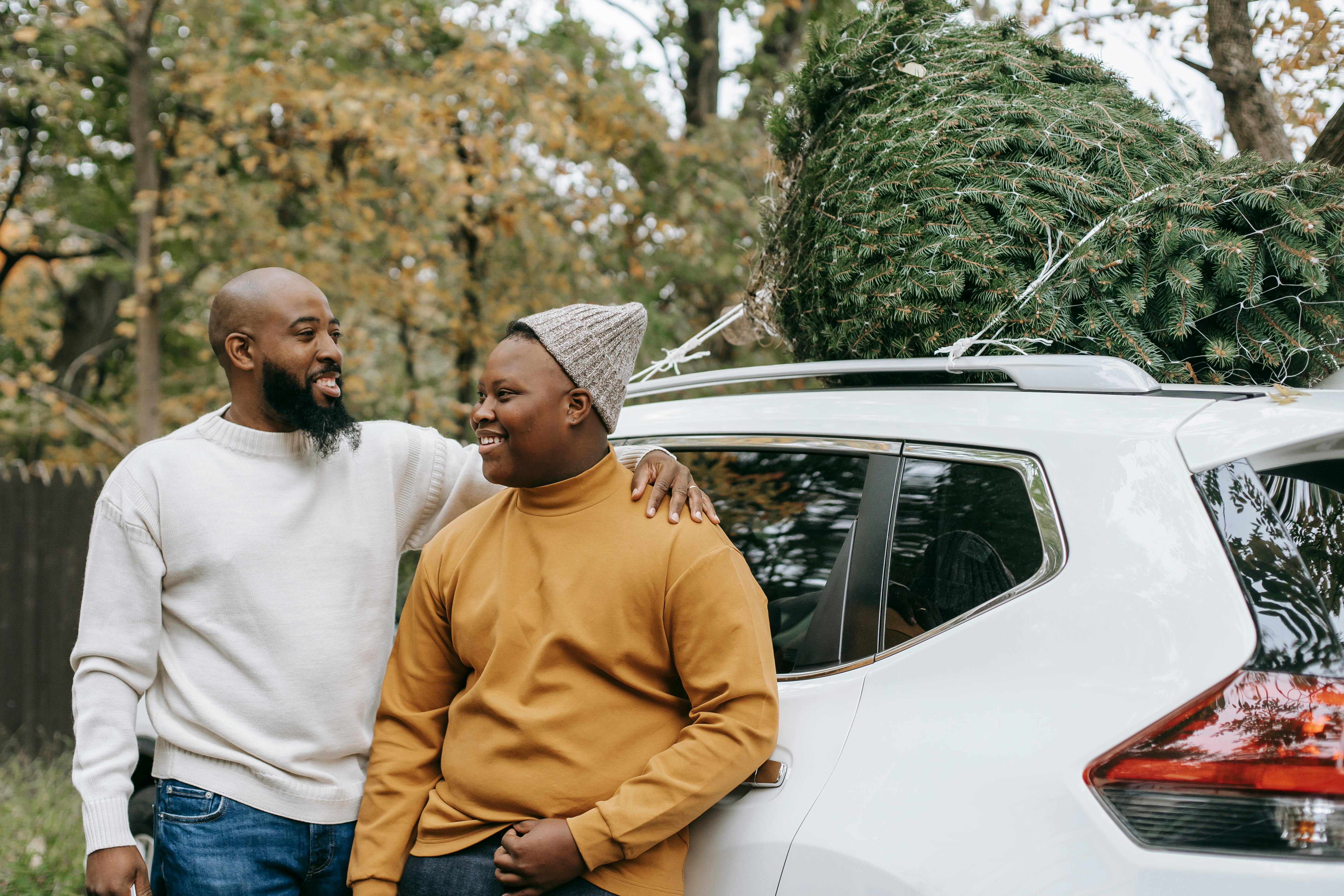 cheerful bearded black father embracing teen near car in countryside