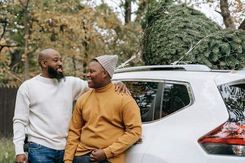 Cheerful bearded black father embracing teen near car in countryside