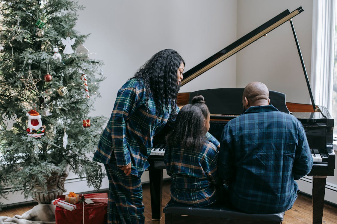 Back view of anonymous African American family playing musical instrument in cozy room with decorated Christmas tree
