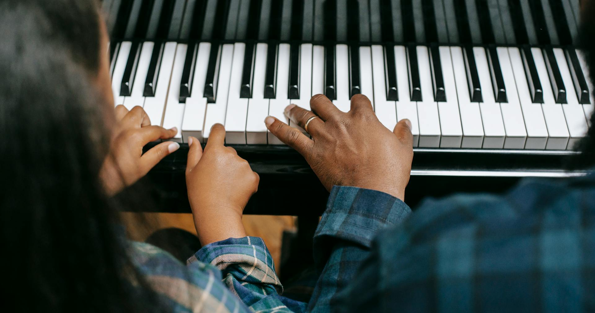 From above of crop anonymous African American man playing musical instrument with girl while rehearsing together