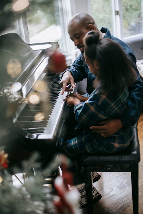 Side view high angle of African American father and daughter playing acoustic piano during Christmas celebration