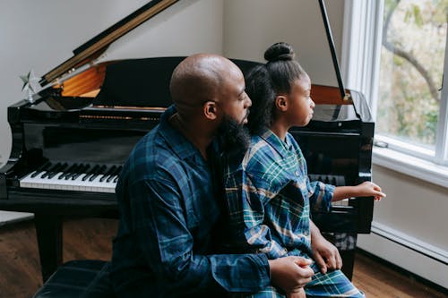 Free Black father and daughter sitting near piano at home Stock Photo