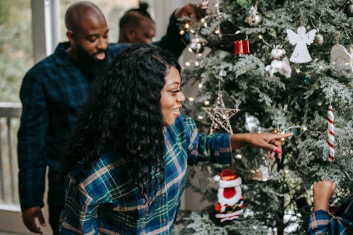 Smiling African American family decorating Christmas tree during New Year holidays in cozy home in winter day