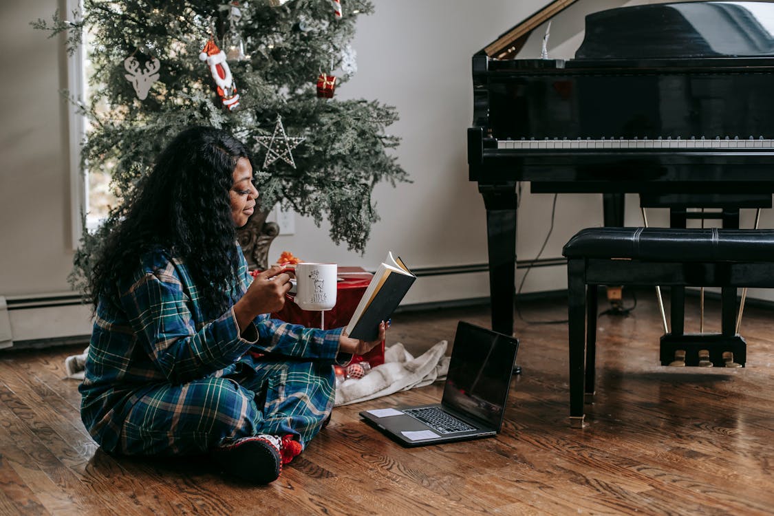 Free Black woman reading book near laptop and Christmas tree Stock Photo