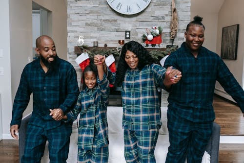 Cheerful African American family smiling happily while holding hands in room with Christmas decorations