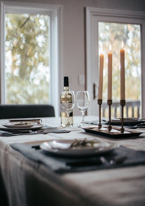 Table with various tableware with bottle of wine glasses and candles placed on tablecloth and prepared for event