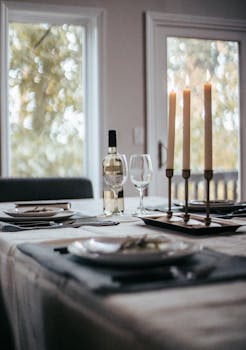 Table with various tableware with bottle of wine glasses and candles placed on tablecloth and prepared for event