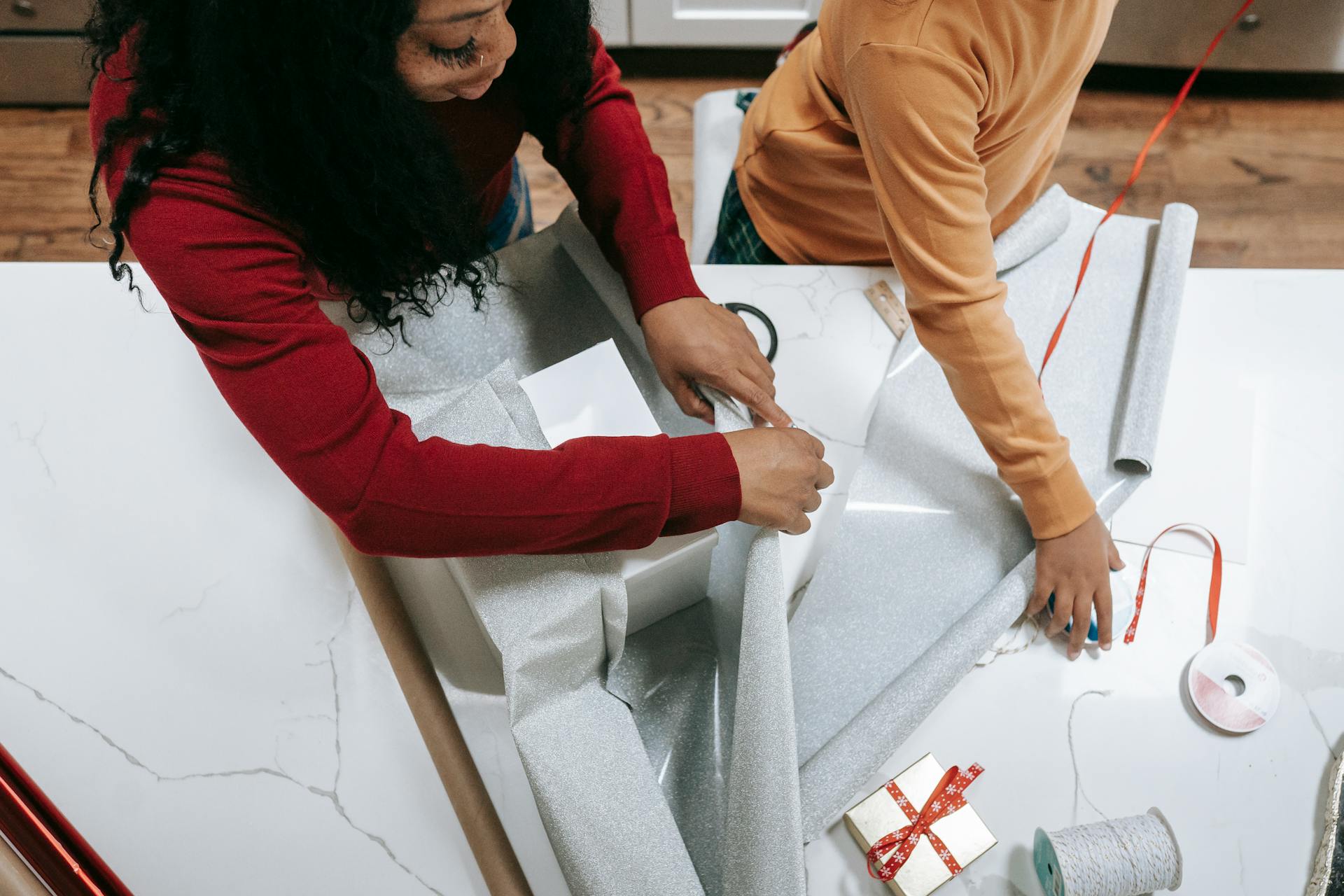 A mother and child bonding while wrapping gifts for the holiday season inside a cozy home.