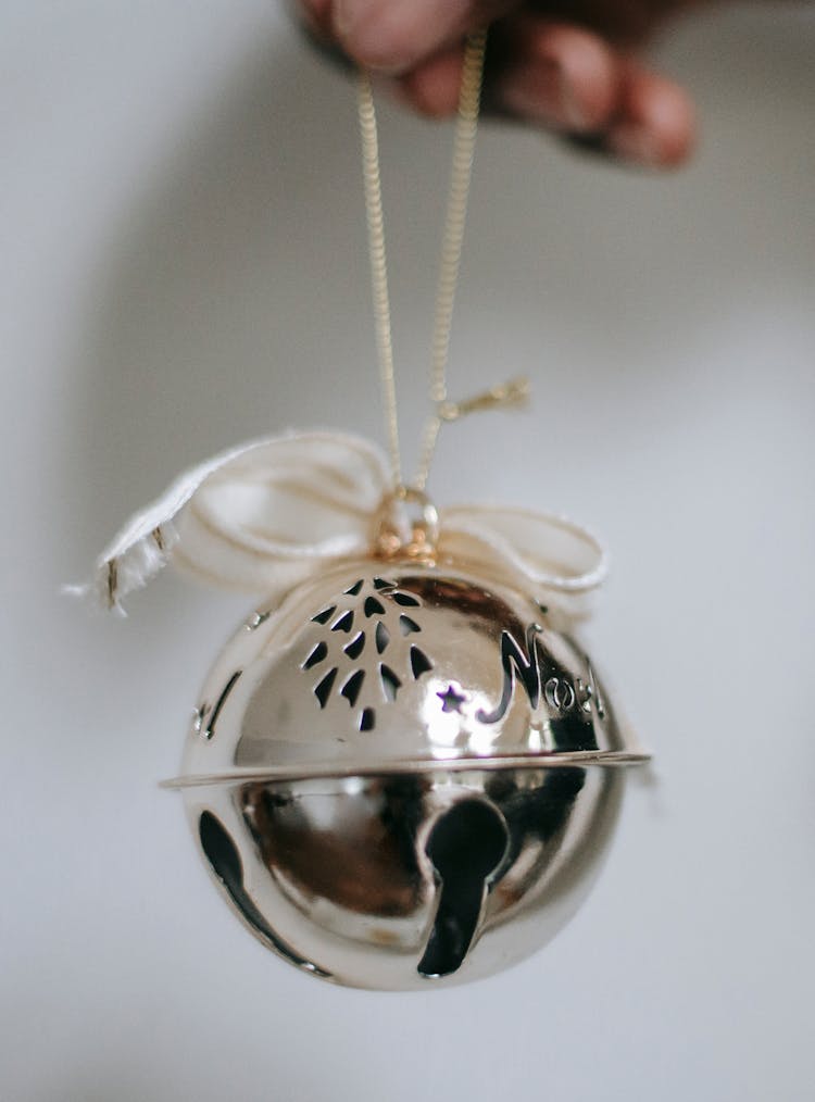 Person Holding Silver Jingle Bell With Ribbon