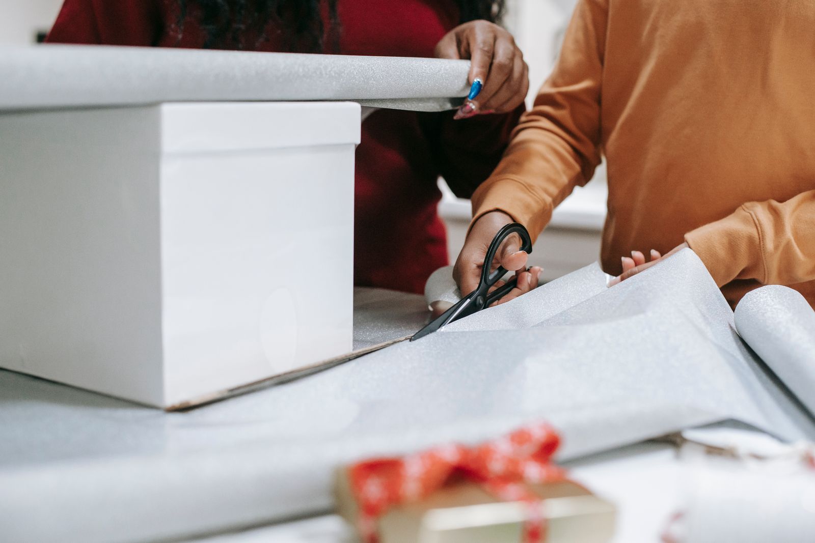 Two people wrapping a Christmas gift with scissors and wrapping paper.