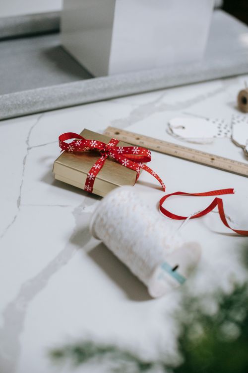 Free From above of small gift box with red ribbon placed near skein of thread and ruler during Christmas preparation Stock Photo