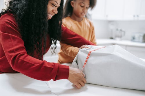 Cheerful crop black mother packing box of gift prepared for Christmas holidays with help of daughter