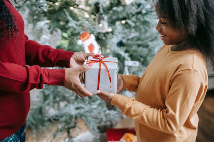 Crop Black Mother Passing Christmas Gift To Smiling Daughter