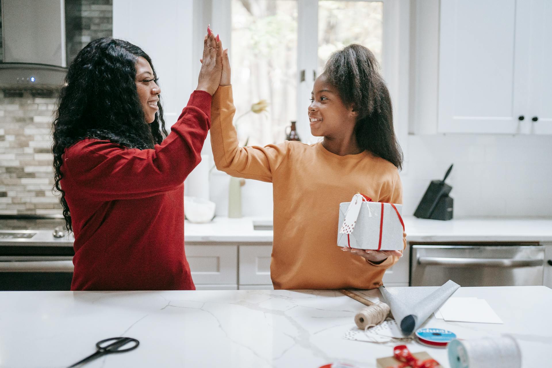 Cheerful black woman and girl giving five at table and looking at each other after wrapping Christmas gift