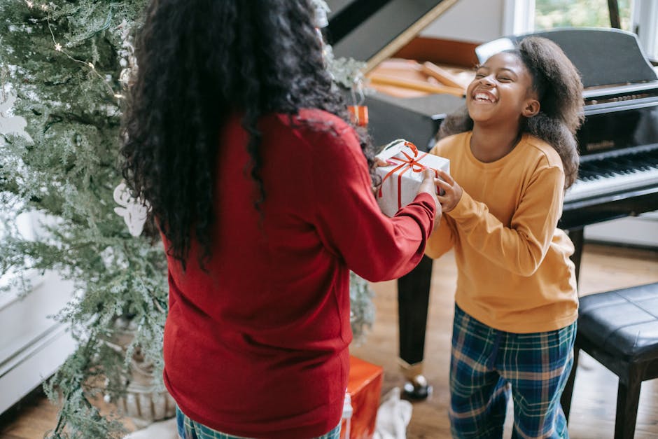 Crop anonymous black woman passing gift box to cheerful daughter during New Year holiday at home