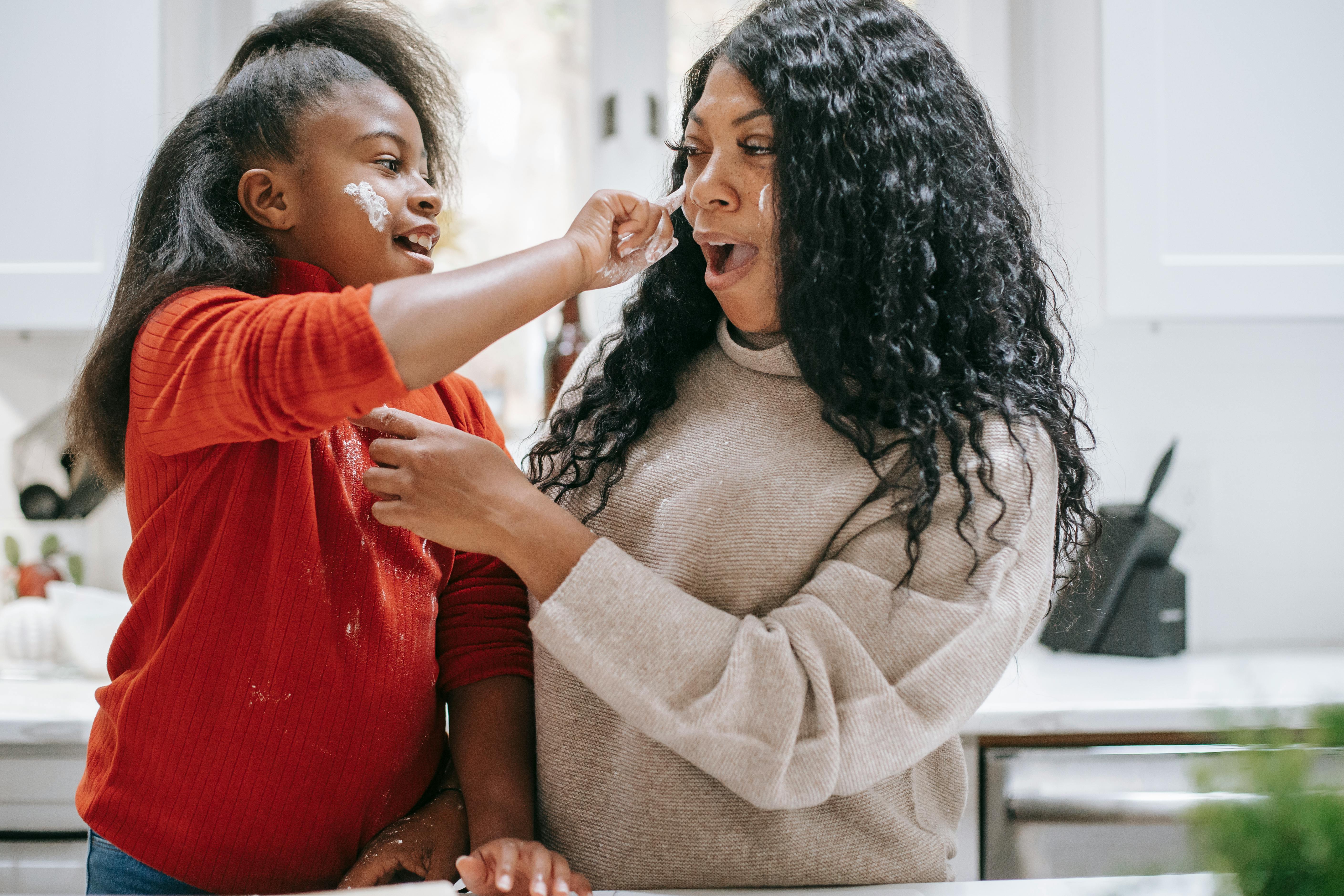 carefree black girl applying flour on face of crop mother