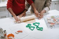 From above of crop unrecognizable ethnic child rolling out dough near parent while preparing gingerbread cookies in kitchen