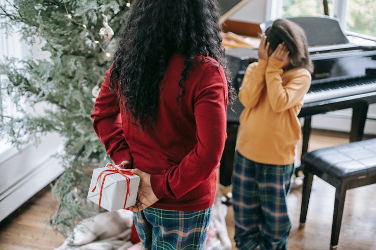 Unrecognizable Black Woman Hiding Gift Box From Daughter