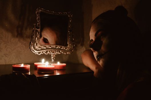 在恐怖的万圣节场景中，一个化着妆、手持蜡烛的女人，倒映在华丽的镜子里