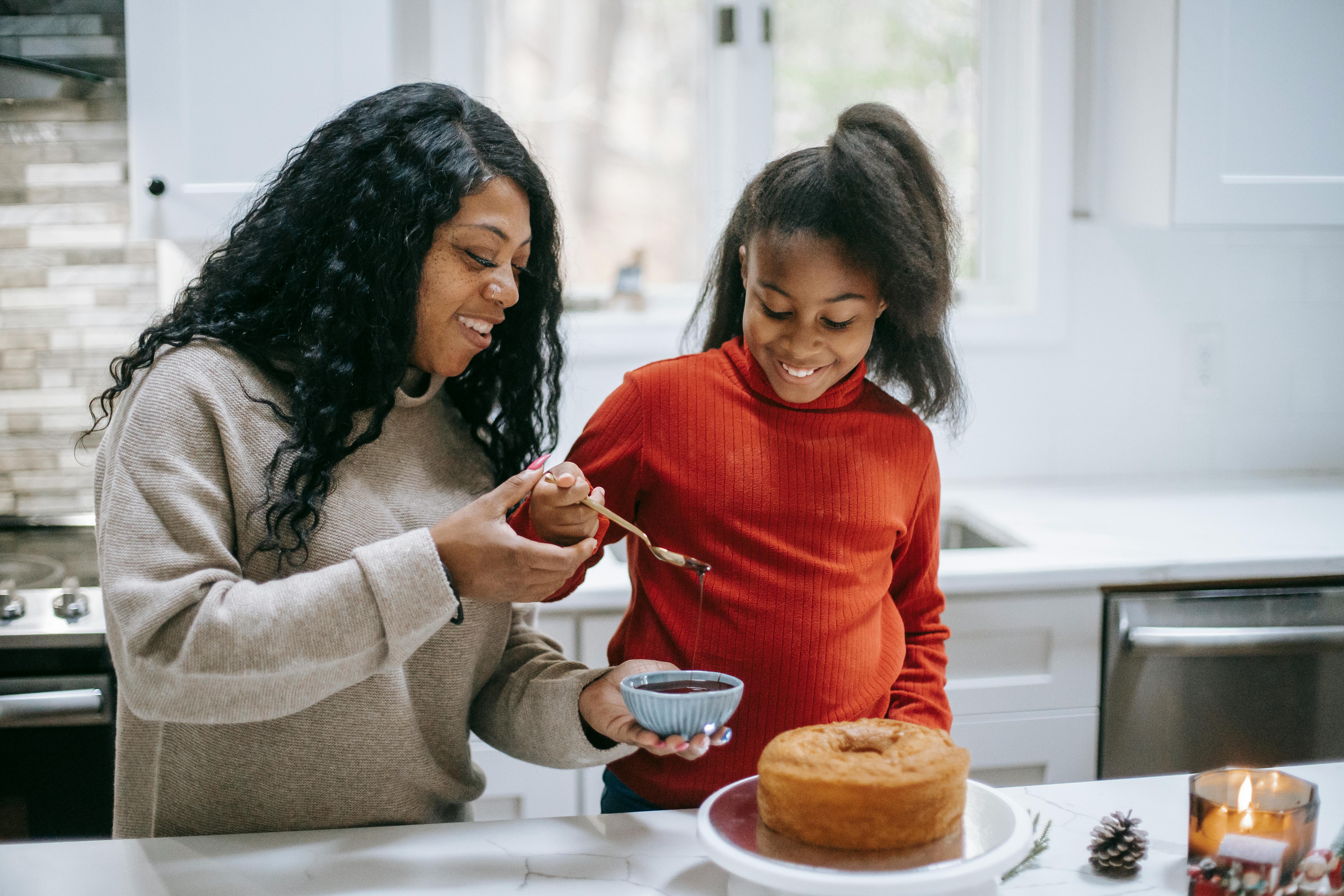 smiling ethnic mother with daughter decorating christmas cake in kitchen