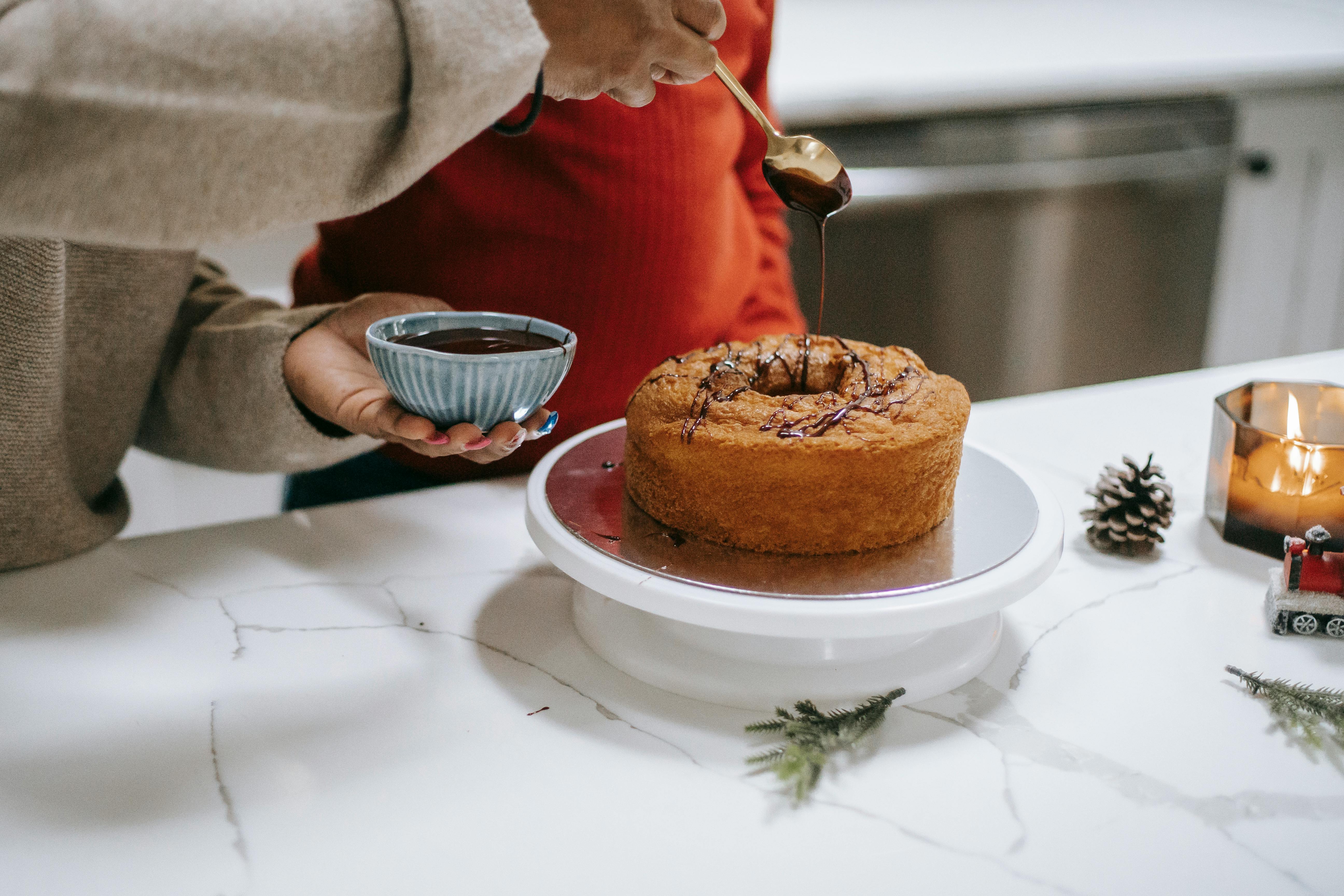 Crop anonymous ethnic parent with kid decorating yummy sponge cake with melted chocolate while preparing for Christmas holiday
