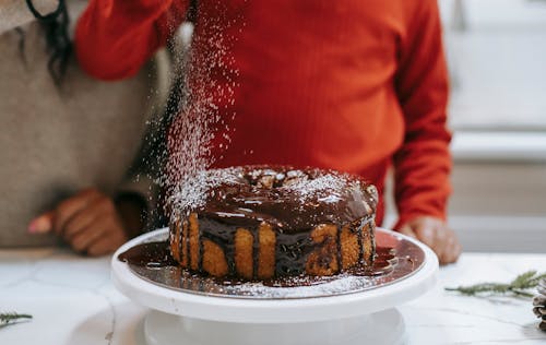 A homemade chocolate cake being decorated with powdered sugar for the holidays.