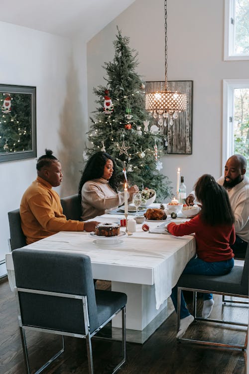 African American parents with anonymous daughter and son dining at table near shiny fir tree in house