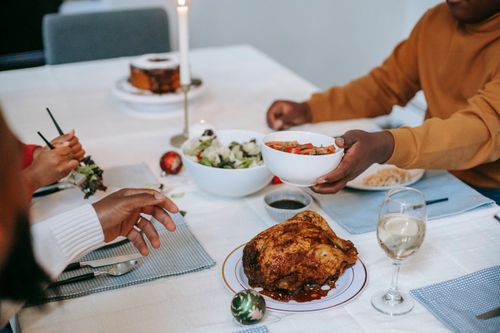 Free From above of crop anonymous African American teen passing bowl with sliced tomatoes to father while celebrating Near Year in house Stock Photo