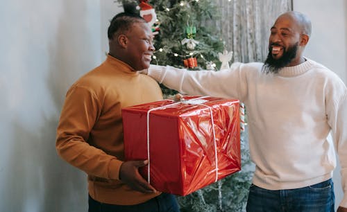 Cheerful African American son receiving present box from happy beaded black father while celebrating Christmas holiday and looking at each other