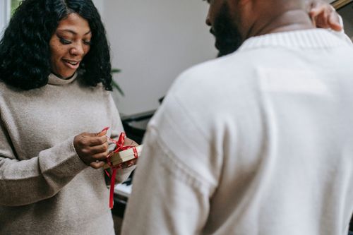 Free Content African American woman opening Xmas present with red ribbon while black man congratulating Stock Photo