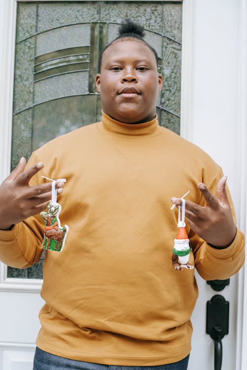 African American adolescent in pullover looking at camera and showing bright small toys on hands near glass door of house