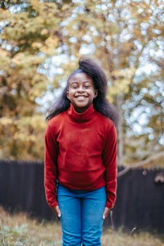 A cheerful girl with curly hair smiling in an autumn yard.