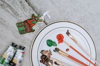 Flat lay of Christmas deer near tubes placed near plate with brushes and mixture of colorful paints