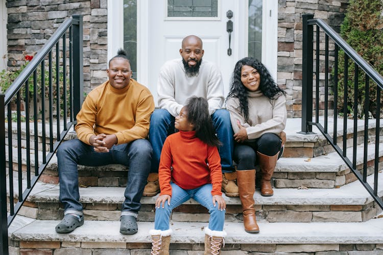 Happy Black Family Sitting On Stairs Of Modern House